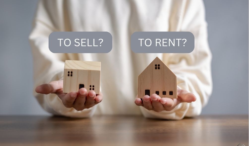 Image description: A person holding two small wooden house models. The left house has a text overlay saying "TO SELL?" and the right house says "TO RENT?"